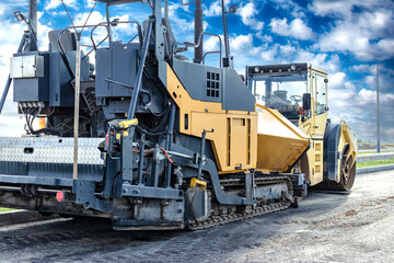 Fototapeta na wymiar Asphalt paving equipment. Asphalt paver against the backdrop of a clear cloudy sky. Construction of new roads and road junctions. Heavy construction industrial machinery.