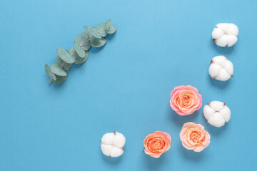 Cotton flowers, pink roses and eucalyptus branch on a light blue pastel paper background. Flower composition. Top view, flat lay, copy space.