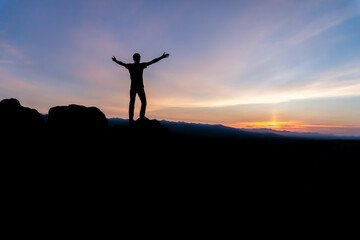 Silhouette of a winner man standing on a mountain. The concept of sports and active life. 