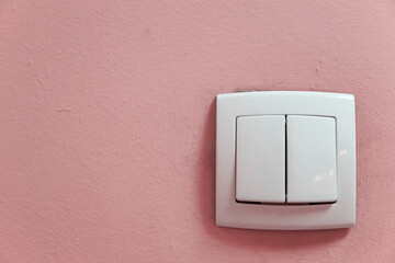 Interior plastic push switch with two buttons on the rough painted wall of the room