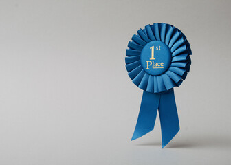 Blue rosette first place on a gray background as a reward for achievement, success and victory.