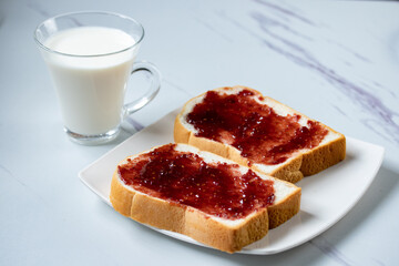 Sliced bread spread with red raspberry jam and fresh milk