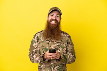 Military Redhead man over isolated on yellow background sending a message with the mobile