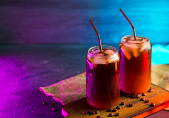 cold brew cold coffee in tall glasses with cream and roasted coffee beans. neon style backlight...