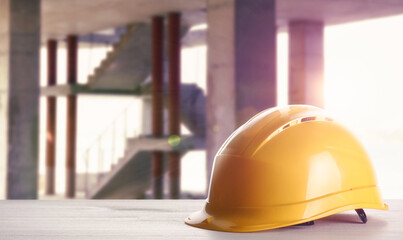 Hard hat on white wooden surface at construction site with unfinished building. Space for text