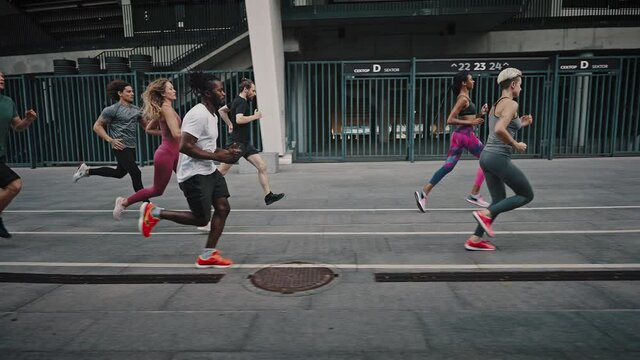 Side view of enduring and attractive athletes of different genders and races running a marathon through the city streets. Sports life and activities