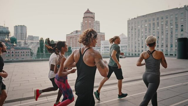 Preparation for sports activities. Portrait of young endurance runners, men and women in sports uniforms having a group training session at the city stadium