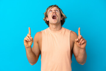 Handsome blonde man isolated on blue background surprised and pointing up