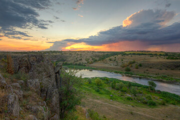 Naklejka na ściany i meble Landscape of the river and granite rocks. Beautiful sunset sky with large clouds.