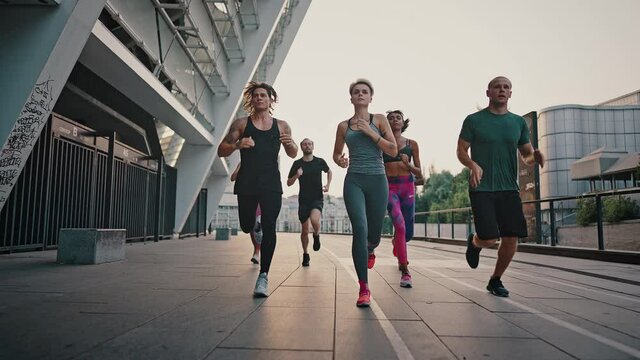 Running club. Multiracial team of like-minded people running through the city streets. People in sports uniforms and shoes have a group workout