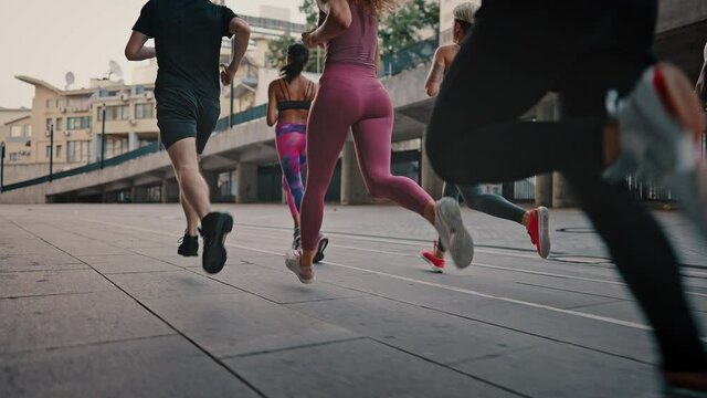 Close-up of legs of athletes in sports shoes. Rear view athletes runners train in the stadium. Young team of man and woman in sportswear. Like-minded club
