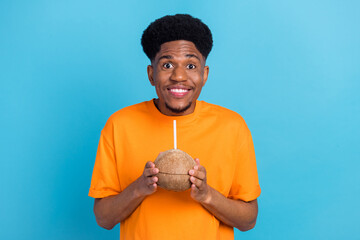 Photo of amazed happy afro american young cheerful man hold hands coconut cocktail isolated on blue...