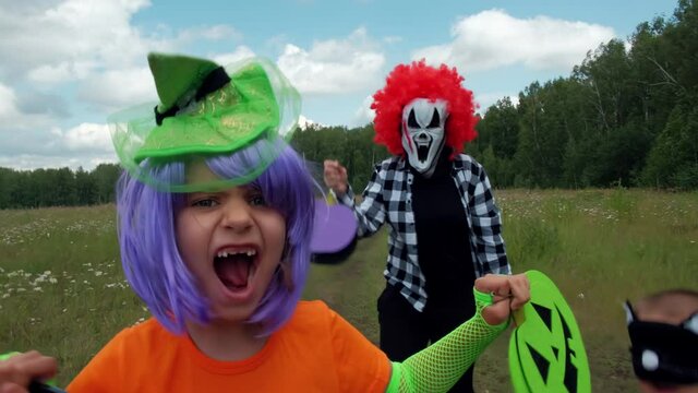 Child in costumes of a clown, a witch and a cat on Halloween run through the forest for sweets. Trick-or-treating.