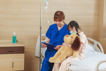 Young Asian female caregiver holding protective face mask with cute girl patient in hospital. Nurse...