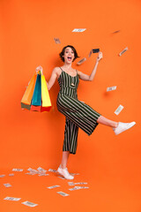 Full size photo of young girl happy positive smile fly money rich shop bags credit card isolated over orange color background
