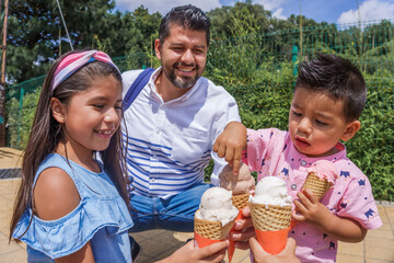 Adult Hispanic man eating ice cream with his children in a park