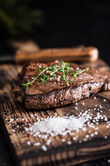 steak on a wooden board with a salt on a dark background