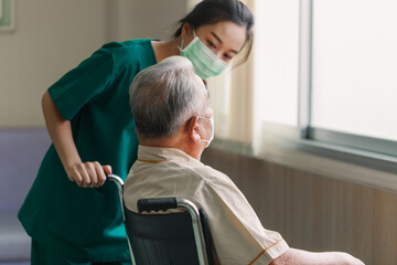Young Asian woman nurse explaining information to elderly man patient in wheelchair with friendly smiley face in the hospital. Young Assistance with old people in the elderly care place