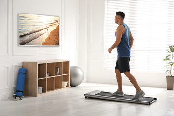 Sporty man training on walking treadmill and watching TV at home