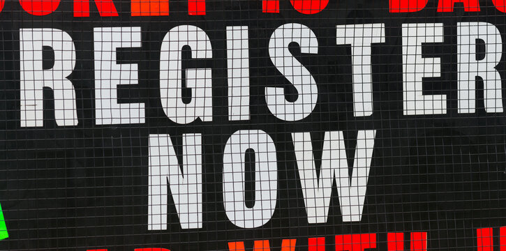 bold sign with the words "register now" in white capital letters on black (with a protective mesh over)