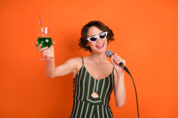 Photo of young attractive girl happy positive smile party drink cocktail cheers toast microphone isolated over orange color background