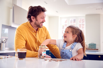 Father And Daughter Counting Pocket Money In Jar On Kitchen Counter