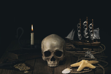 Vintage concept of sea travel. Burning candle, skull , rope, gold coins and shells on the old wooden table. Pirate ship. Sea adventure.