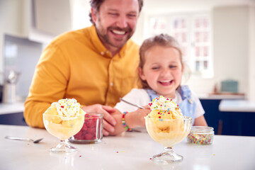 Obraz na płótnie Canvas Father And Daughter In Kitchen Decorating Ice Cream Dessert With Cream And Sprinkles