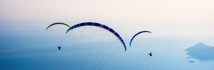 Paraglidirs group are flight over the sea near the Oludeniz coast on sunset. Active leisure,...