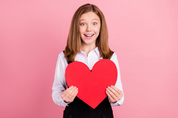 Photo of shiny excited school girl wear white black uniform smiling holding red heart isolated pink color background