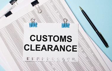 On a light blue background, documents, a pen and a sheet of paper on blue paper clips with the text CUSTOMS CLEARANCE. Business concept.