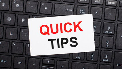 On a black computer keyboard there is a white card with the text QUICK TIPS. View from above