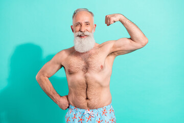 Portrait of attractive cheerful elderly grey-haired bearded man showing muscles isolated over...