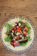 Close up of vegan salad lunch of lettuce pepper apple avocado celery pear cucumber seeds and balsamic vinegar dressing on china plate flat lay view with background of wood kitchen surface in day light