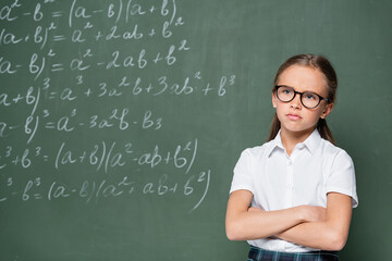 offended schoolgirl standing with crossed arms near chalkboard with equations