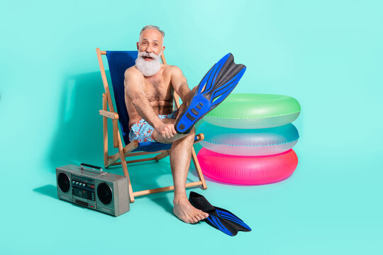 Photo of pretty cute retired man naked torso sitting beach chair wearing flippers listening boombox isolated turquoise color background