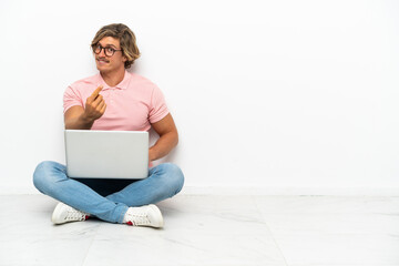 Young caucasian man sitting on the floor with his laptop isolated on white background doing coming gesture