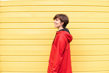 Photo of a young girl with a red raincoat smiling with a yellow background behind her.