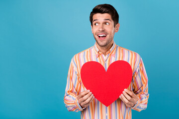 Photo of positive young happy man look empty space amazed hold heart smile isolated on blue color background