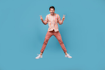 Fototapeta na wymiar Full length photo of young cheerful man happy positive smile jump show peace v-sign isolated over blue color background