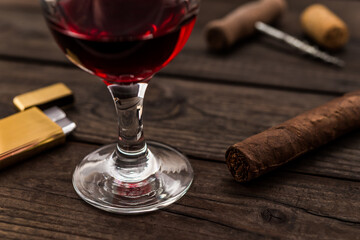 Glass of red wine and cuban cigar with corkscrew and corks on an old wooden table. Close up view,...