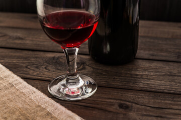 Glass of red wine with bottle of red wine and piece of canvas on an old wooden table. Angle view, focus on the glass of red wine