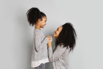 Mother and daughter looking each other in eyes on grey background.