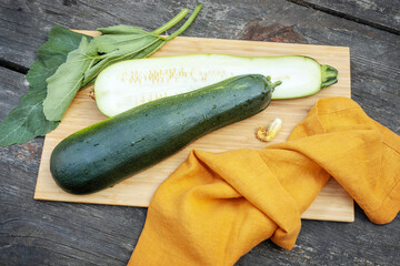 Summer, eco friendly composition with cut in half, green zucchini with leaves, flower and napkin on a kitchen board on a wooden background. Locally grown vegetables and sustainable eating concept