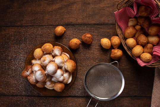 Brazilian sweet called "bolinho de Chuva", dumplings on a glass plate covered with sugar, over rustic wood, top view.