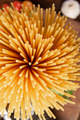 Italian pasta (macaroni), spaghetti tied with sisal string, tomatoes, olive oil, cheese and spices on rustic wood, top view.