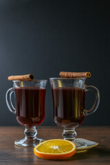 Mulled wine in glass cups with cinnamon and oranges on a wooden table.