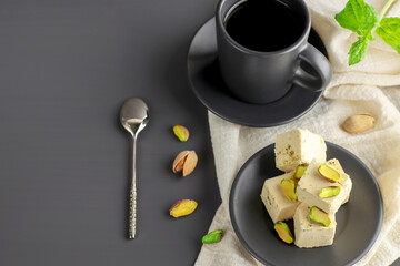 Halva with pistachios on a plate on a dark background. Turkish, Arab and Jewish national sweets. Natural vegan product. Traditional oriental dessert Chekme. Copy space.