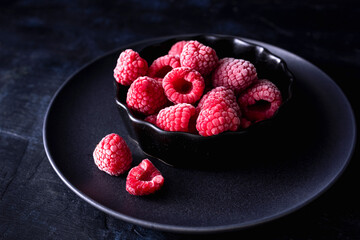 Raspberries in a bowl and dark background. Frozen fruit. Moody photograph of frozen raspberries