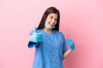 Dentist woman holding tools isolated on pink background with thumbs up because something good has happened